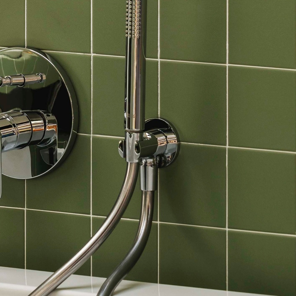 Lifestyle image of the Roca Aqua Chrome Wall Bracket & Outlet mounted on a green tiled bathroom wall with handset shower